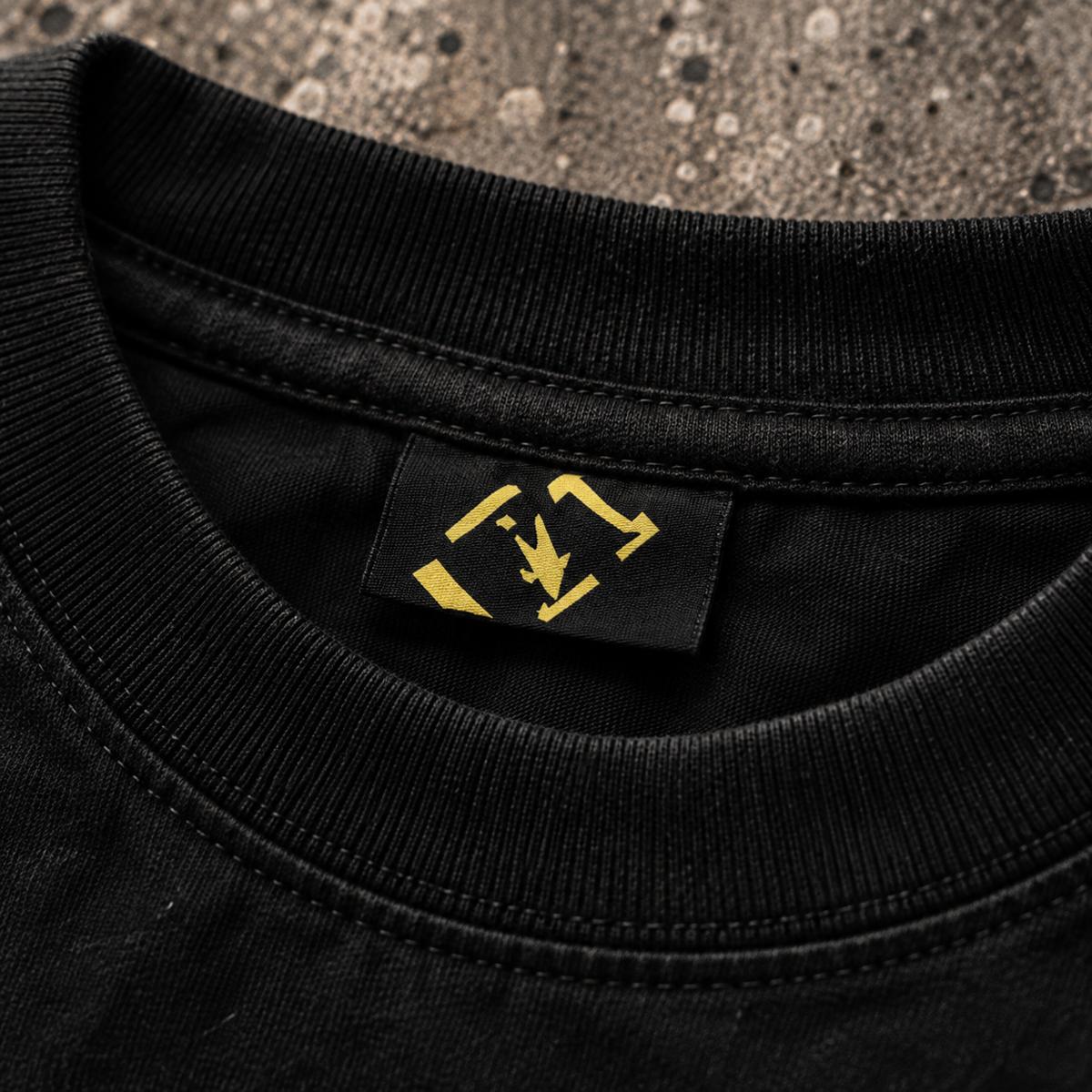 Neck-Label des In 4X We Trust Tee in Nahaufnahme, gelbes 4X-Zeichen auf schwarzem Stoff
