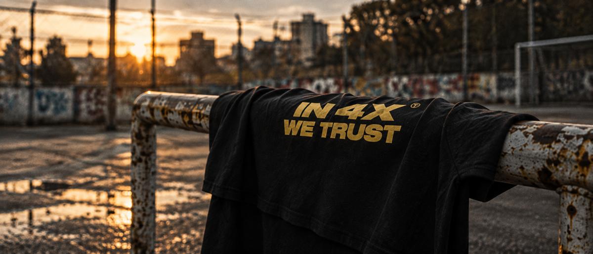 In 4X We Trust Tee vor Maschendrahtzaun, Querformat